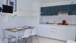 A compact kitchen with white cabinets, a gas stove, a sink, and a dining area with two chairs and a table. - Pozzo al Moro Village (Campo nell'Elba)