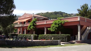 A two-story building with a red facade, a balcony, and a staircase leading to the upper floor. - Pozzo al Moro Village (Campo nell'Elba)