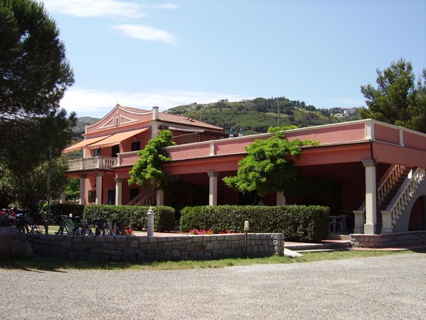 A two-story building with a red facade, a balcony, and a staircase leading to the upper floor. - Pozzo al Moro Village (Campo nell'Elba)