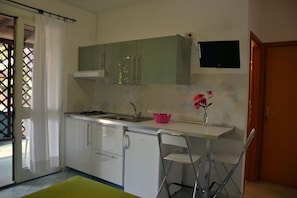 A compact kitchen with white cabinets, a sink, and a small dining area with a chair. - Pozzo al Moro Village (Campo nell'Elba)