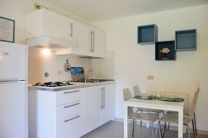 A compact kitchen with white cabinets, a gas stove, and a dining area with a table and chairs. - Pozzo al Moro Village (Campo nell'Elba)