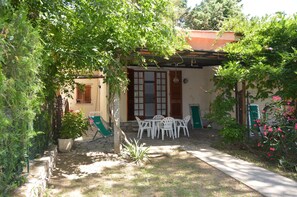 A covered outdoor seating area with a table and chairs, surrounded by greenery and a stone pathway. - Pozzo al Moro Village (Campo nell'Elba)