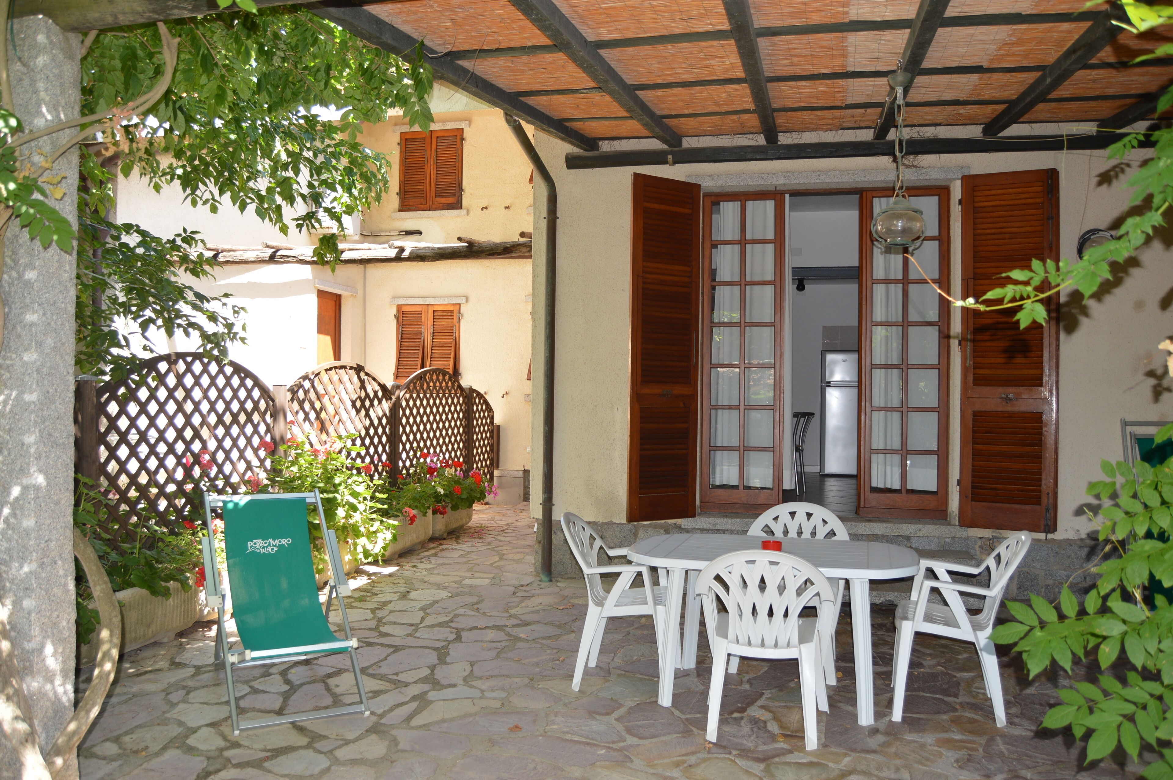 Un patio con pavimentazione in pietra, arredi da esterno bianchi, persiane in legno e un lampadario.