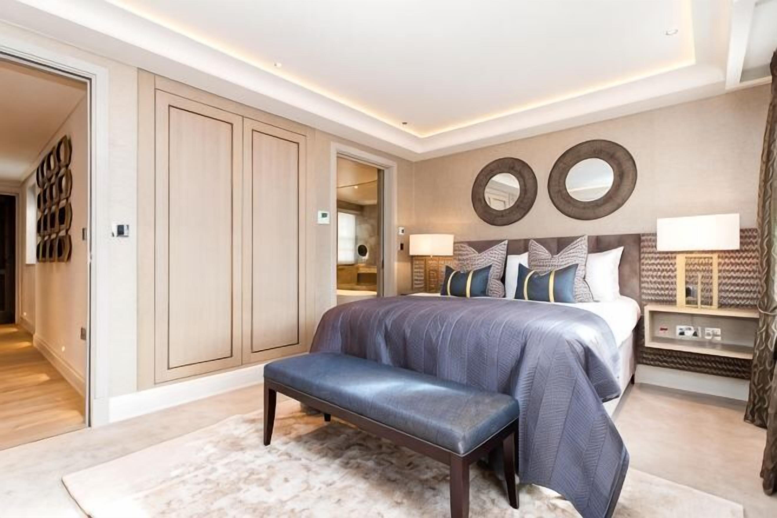 Ein Schlafzimmer mit einem großen Bett, einer Bank, einem Kleiderschrank und einem Spiegel an der Wand.