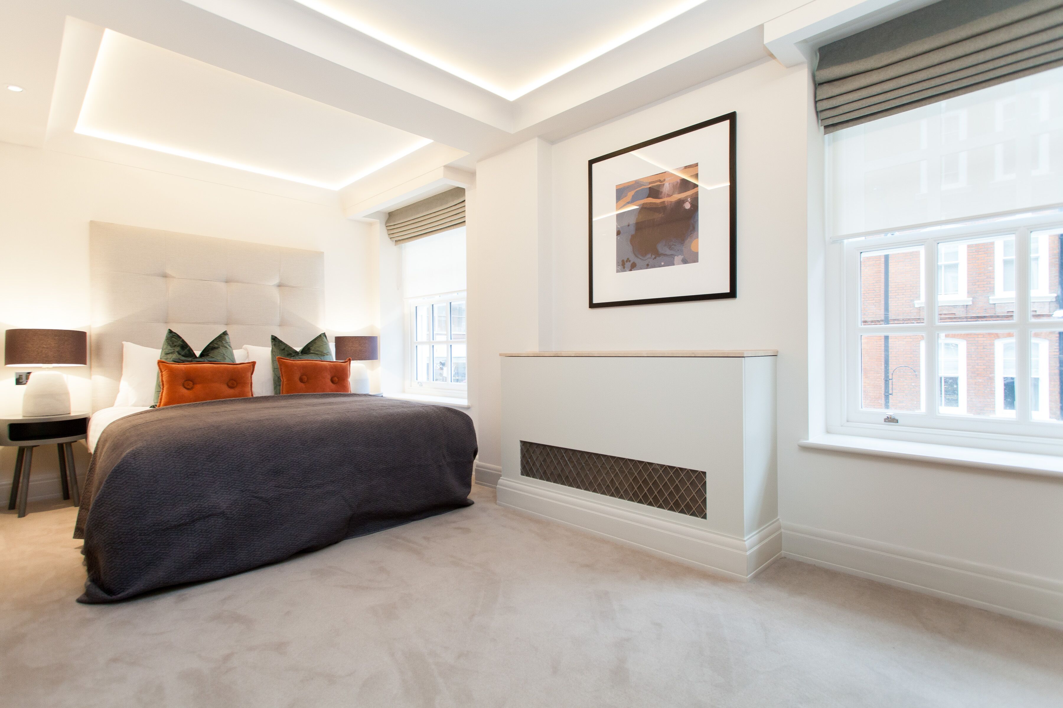 A modern bedroom with a large bed, a bedside table, a chair, and a window with blinds.