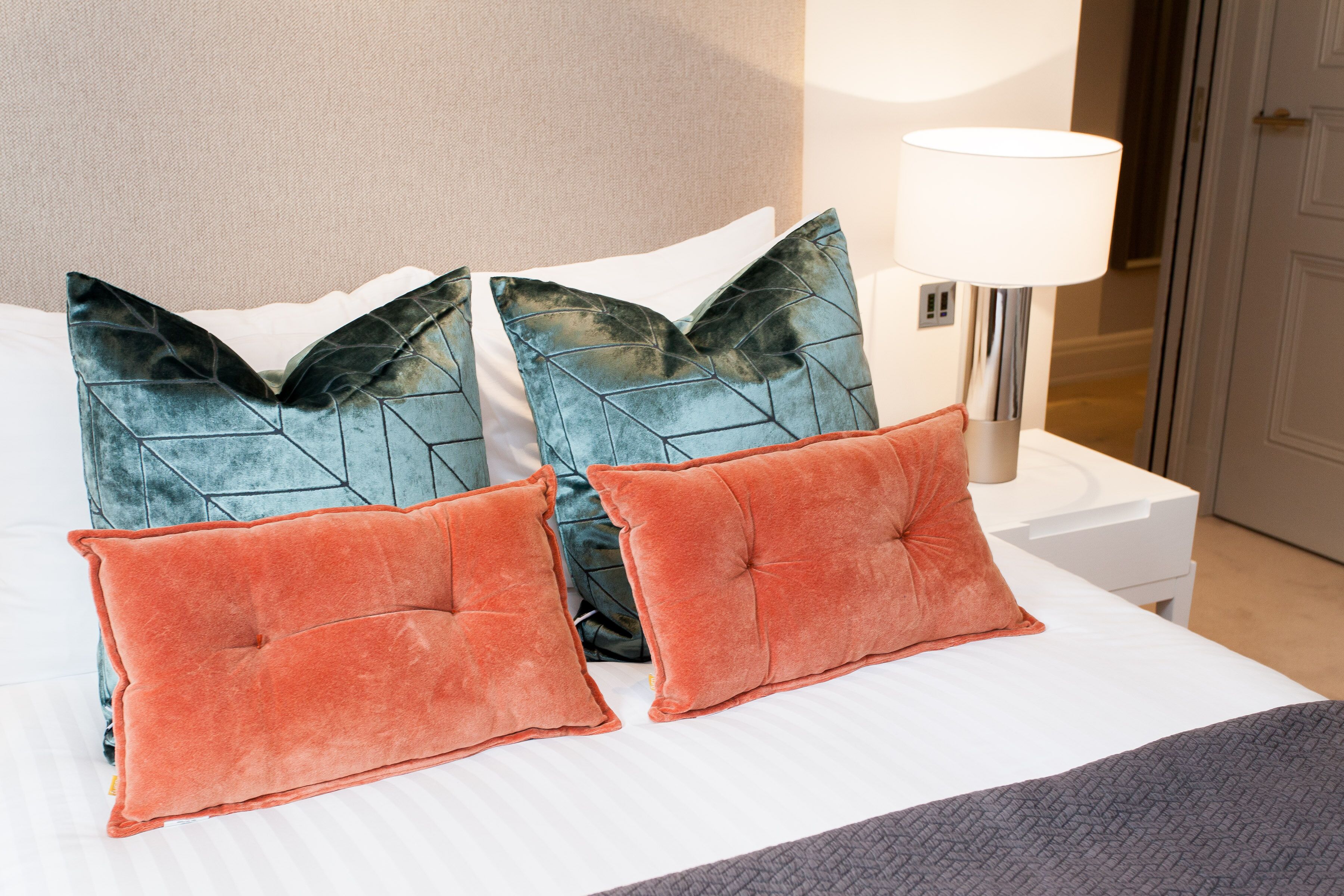 A neatly made bed with two decorative pillows, a bedside lamp, and a white nightstand.