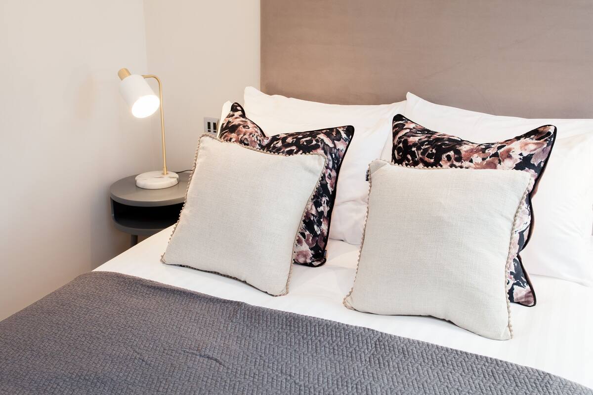 A neatly made bed with two pillows, a bedside lamp, and a grey blanket.