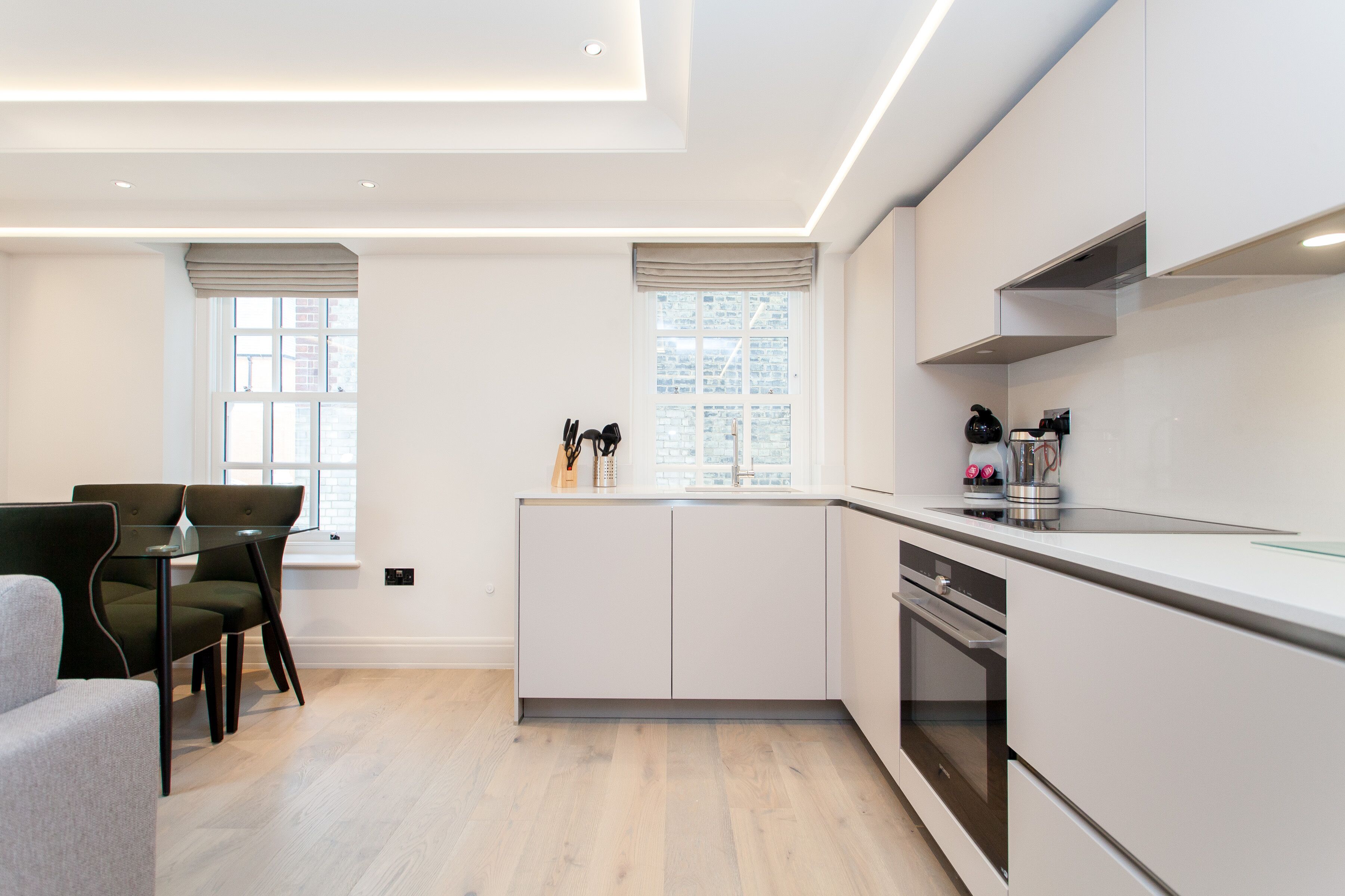 A modern kitchen with white cabinetry, a built-in oven, and a dining area with a glass table and chairs.