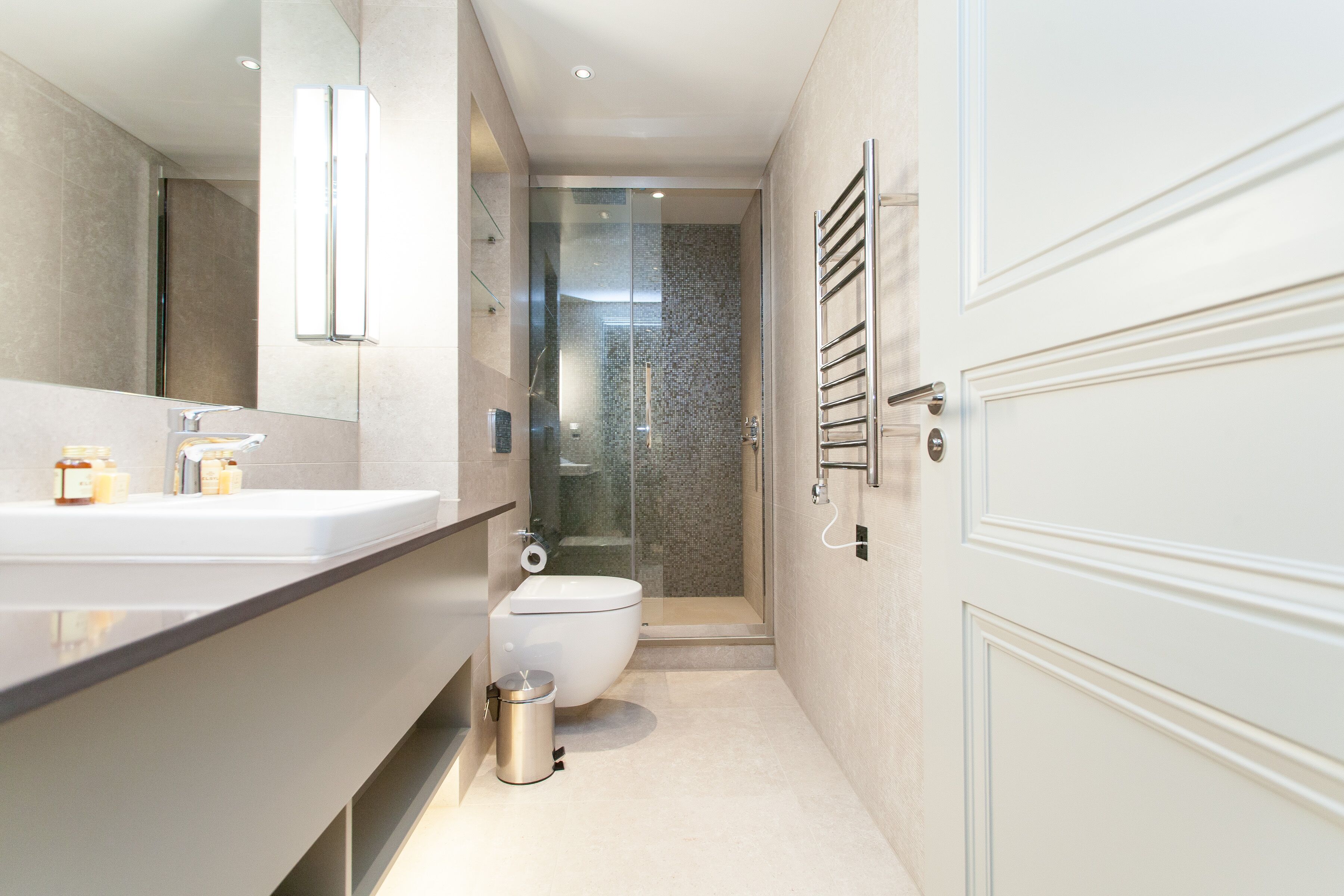 Une salle de bain moderne avec un grand miroir, des toilettes, une douche et un porte-serviettes.