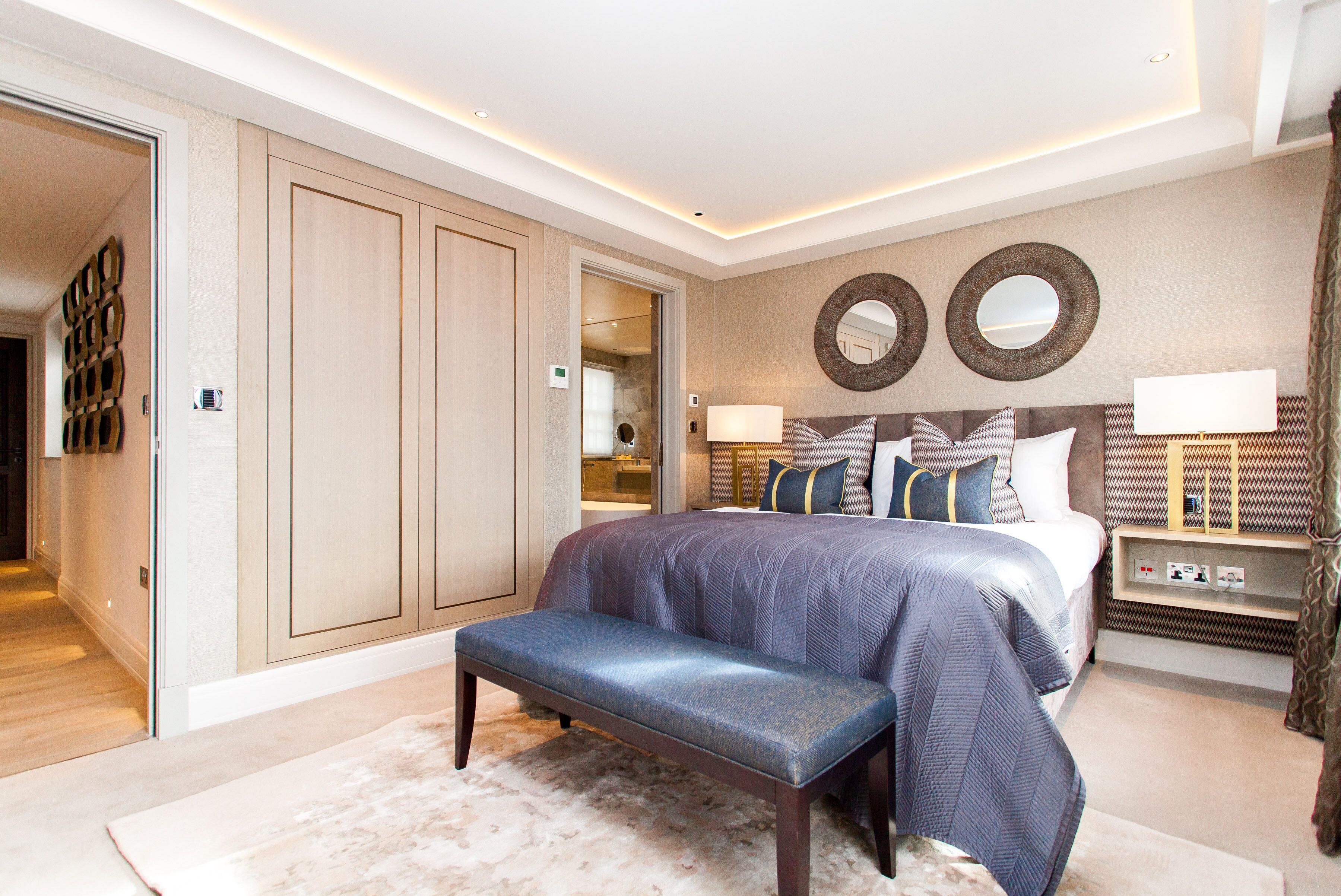 Une chambre à coucher moderne avec un grand lit, un banc, un dressing et une table de chevet avec des lampes.