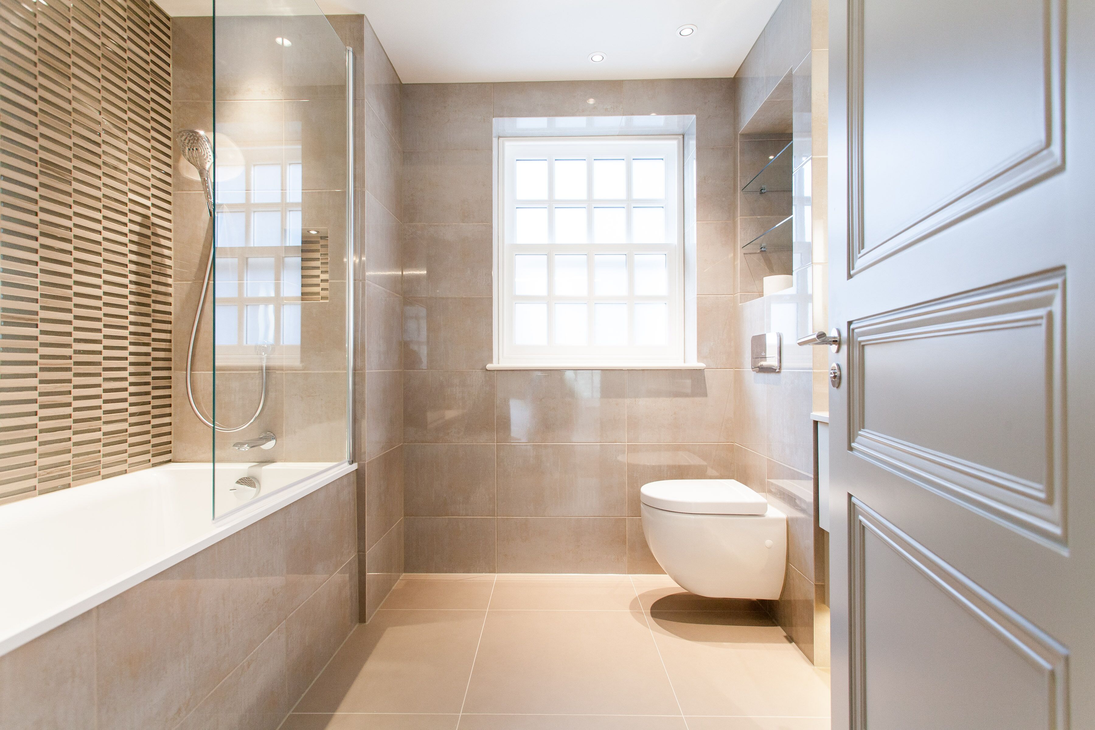 A modern bathroom with a glass-enclosed shower, a toilet, and a window providing natural light.