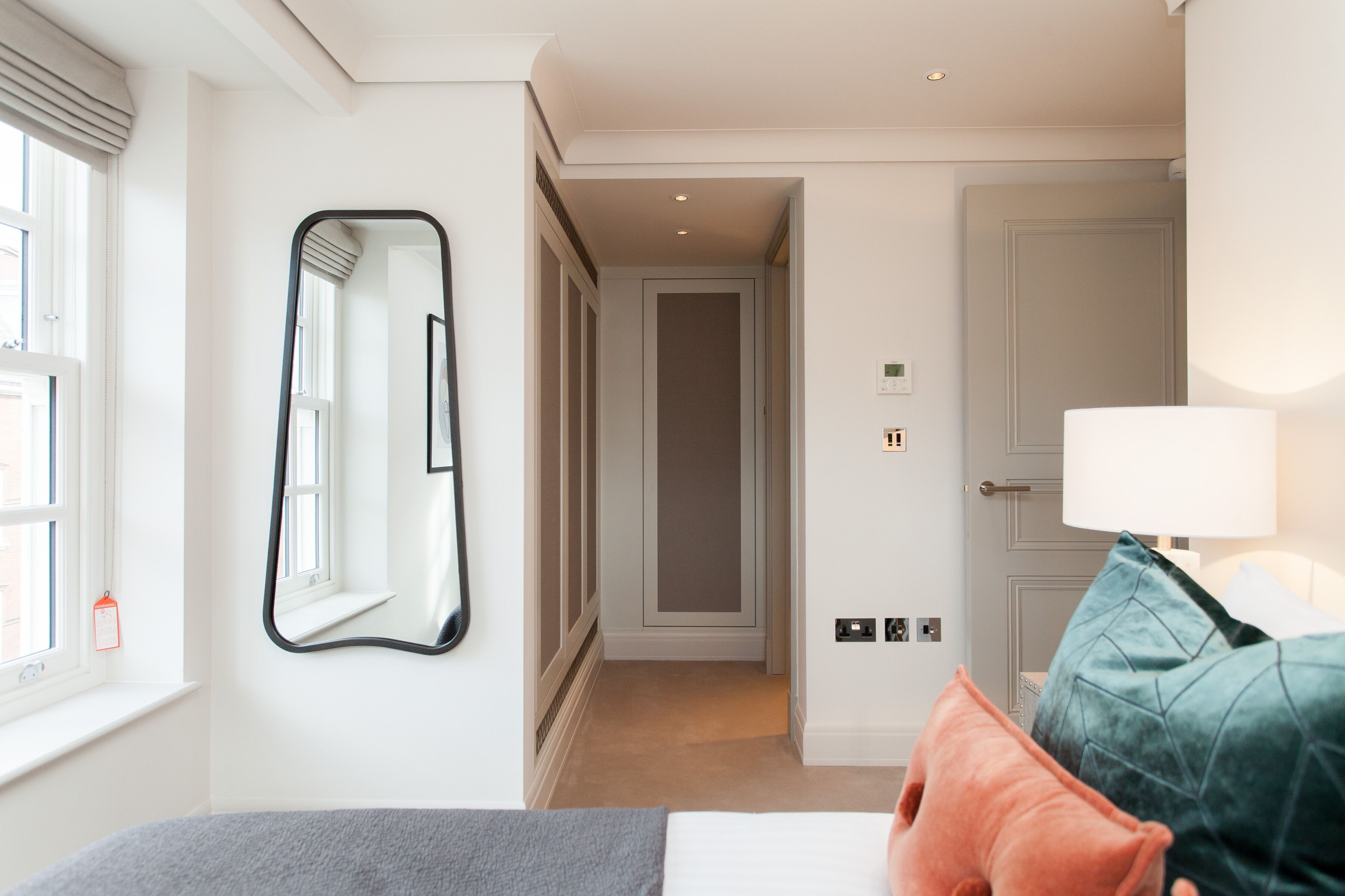 Una habitación de hotel con cama, espejo, ventana, puerta y lámpara.