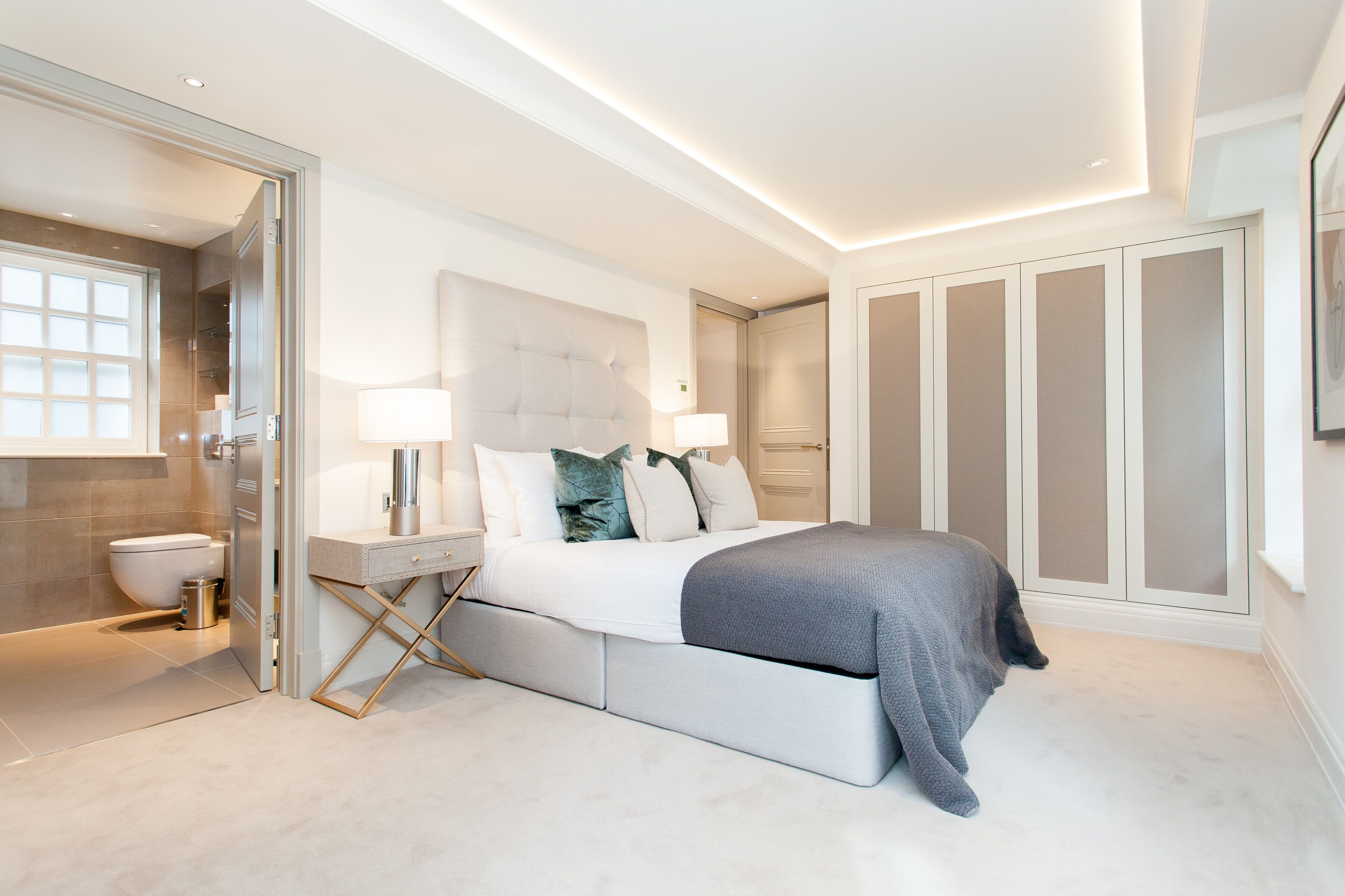 A modern bedroom with a large bed, bedside tables, a walk-in closet, and a bathroom with a toilet and shower.