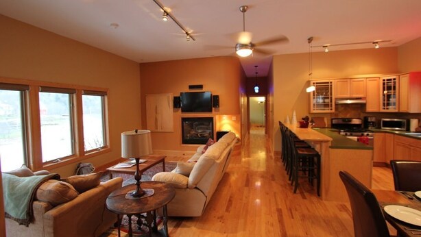 A spacious living area with a sofa, coffee table, and dining table. A kitchen with wooden cabinets and appliances is visible in the background. - Quiet Modern Luxury Home w/ Memory Foam Beds, FAST WiFi and Full Kitchen (Bridgewater)