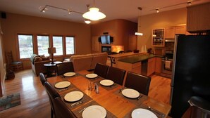 A modern kitchen with wooden cabinets, a dining area with a table set for four, and a living area with a sofa and a TV. - Quiet Modern Luxury Home w/ Memory Foam Beds, FAST WiFi and Full Kitchen (Bridgewater)
