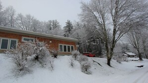 A snow-covered residential area with a brick house, a red car, and bare trees. - Quiet Modern Luxury Home w/ Memory Foam Beds, FAST WiFi and Full Kitchen (Bridgewater)