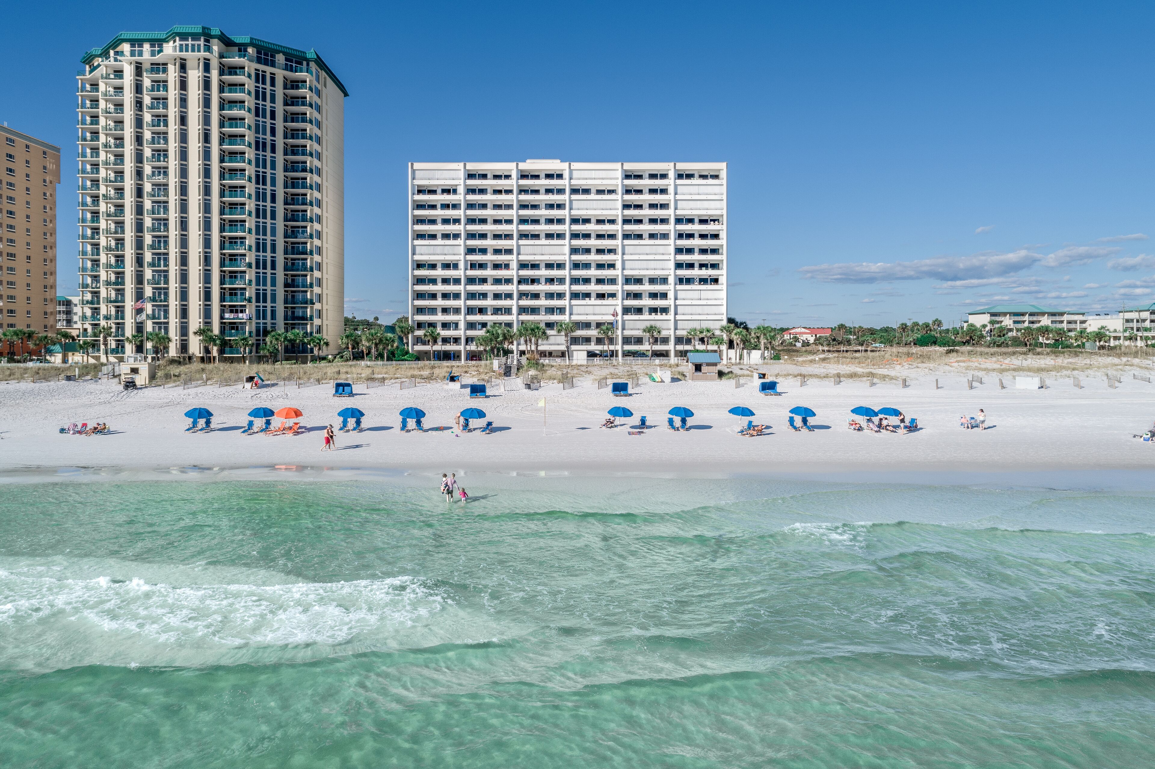 A beach with clear turquoise waters, a sandy shore, and several blue umbrellas.