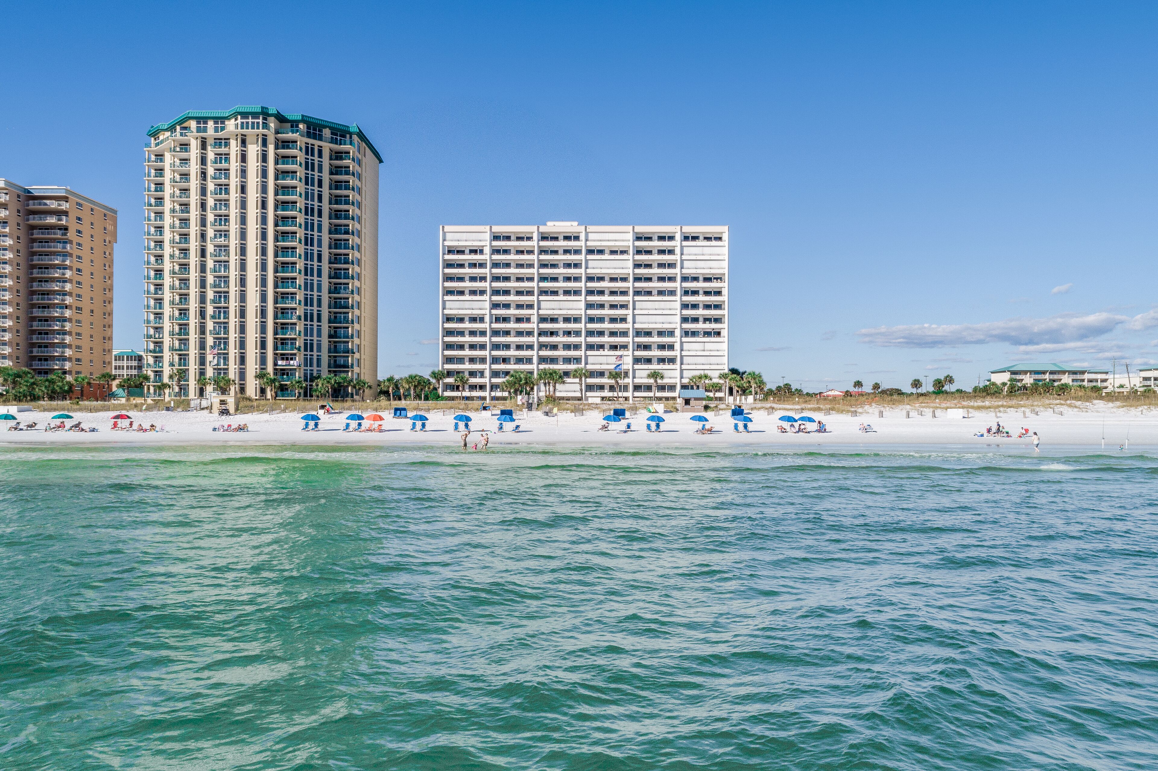 A beachfront hotel with a pool, beach umbrellas, and a view of the ocean.