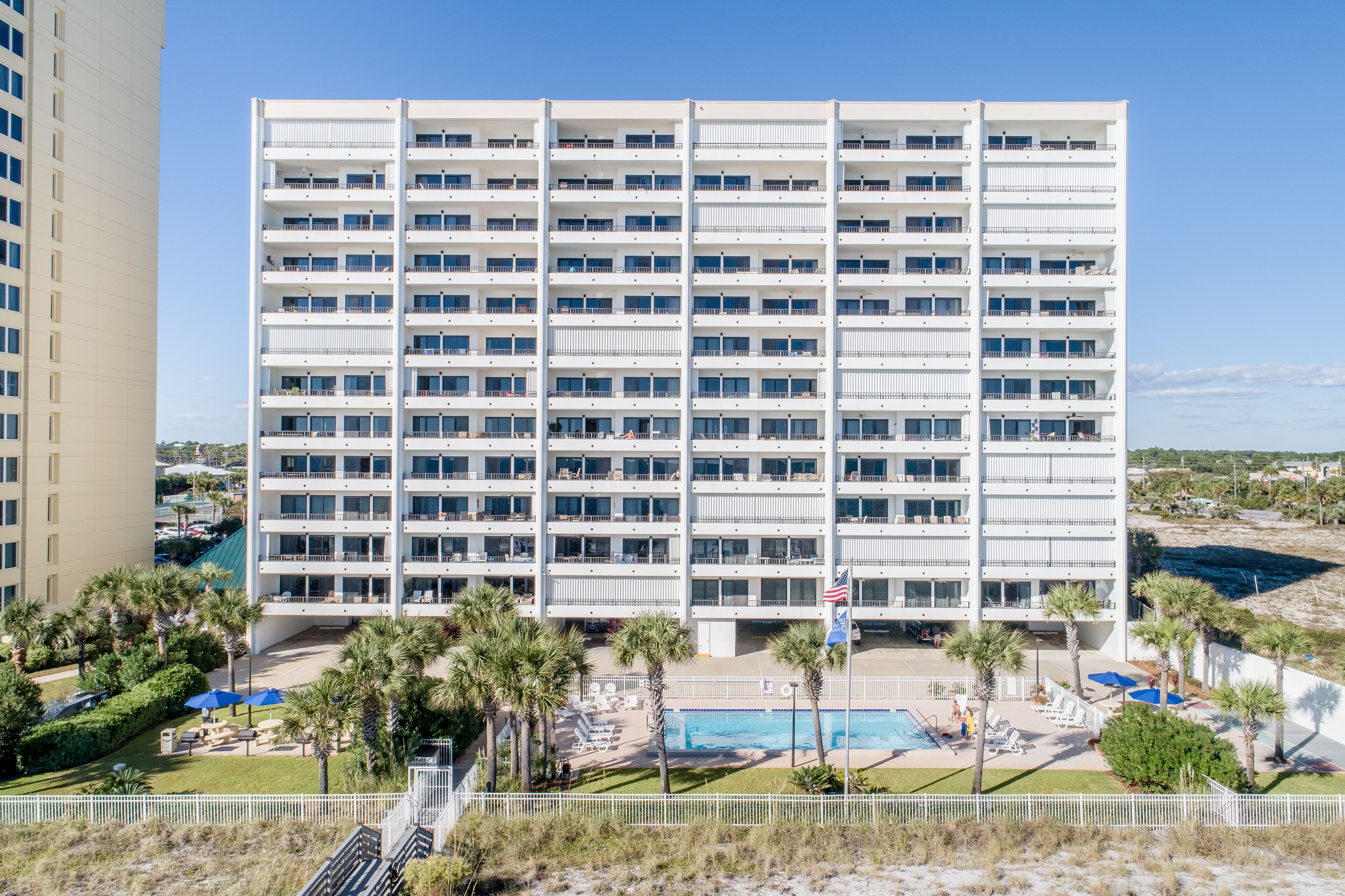 A multi-story hotel with a pool area, outdoor seating, and palm trees.