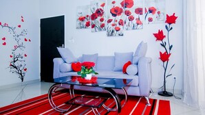 A modern living room with a grey sofa, a glass coffee table, and a red and black striped rug. - Complexe Hôtelier Akparo (Dabou)