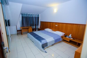 Hotelkamer met een bed, nachtkastje, bureau, stoel en een raam met gordijnen.