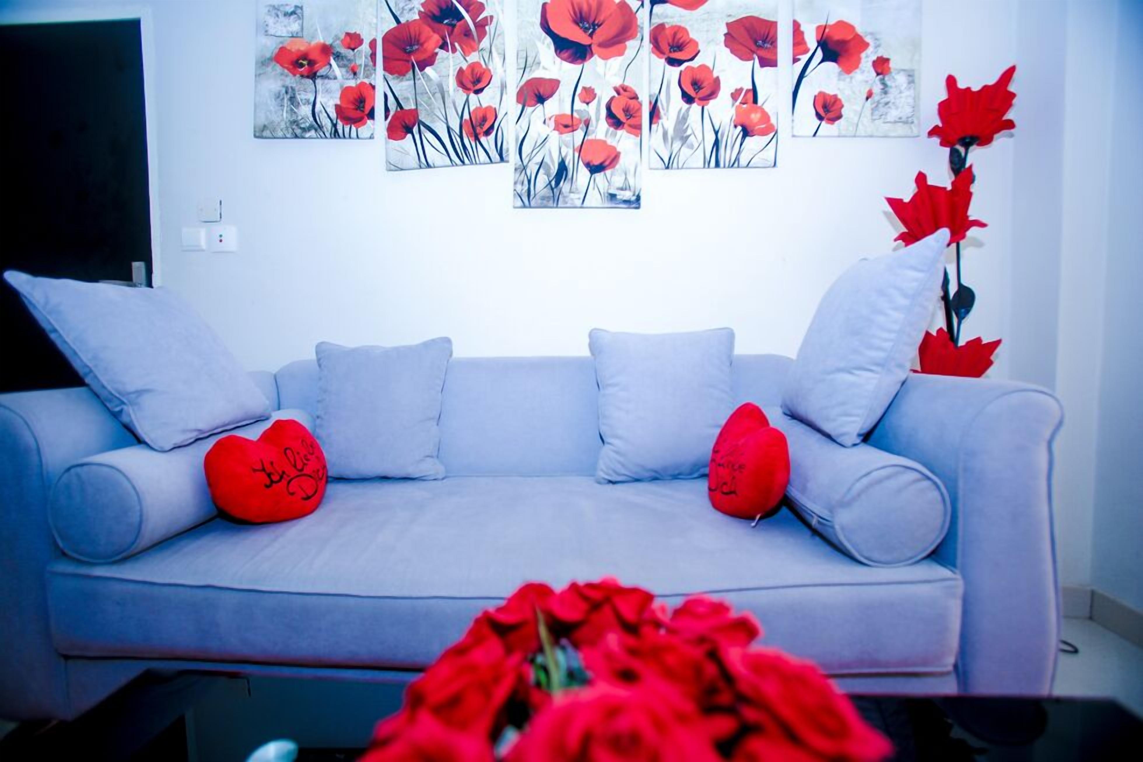A living room with a light blue sofa, two red heart-shaped cushions, and a wall art of red poppies.