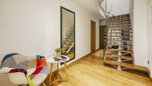 Un salon moderne avec un plancher en bois, un escalier en bois à plusieurs niveaux, un grand miroir et une petite table sur laquelle est posée une plante.