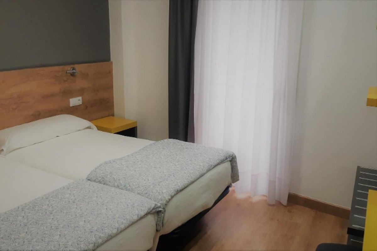 A hotel room with a double bed, a wooden headboard, a bedside table, and a window with curtains.