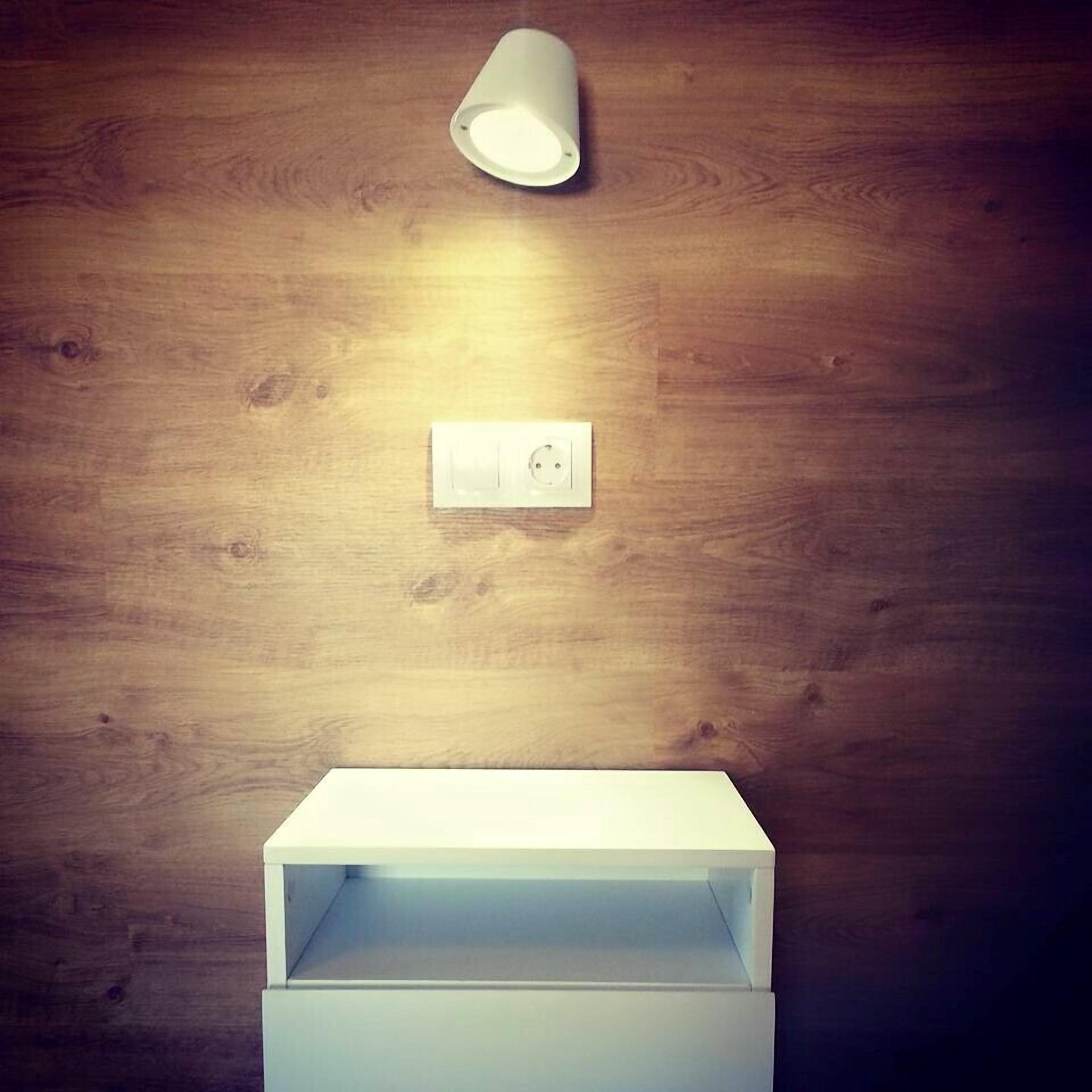 Un baño con pared de madera, un lavabo blanco y una lámpara sobre el espejo.