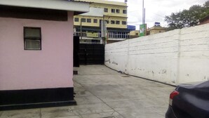 Un estacionamiento con suelo de hormigón, un edificio rosa y una pared blanca.