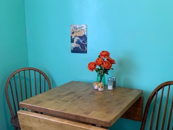 A wooden table with a vase of red flowers, salt and pepper shakers, and a card on the wall. - Beach Side Studio #4 - Pet Friendly, WiFi, Off-Street Parking, Large Smart TV (Norfolk)