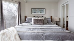 Une chambre à coucher bien rangée, avec un grand lit, un tableau encadré au mur et une fenêtre avec des rideaux.