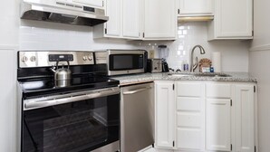 Une cuisine compacte avec des meubles blancs, une cuisinière en acier inoxydable, un four à micro-ondes et un lave-vaisselle.