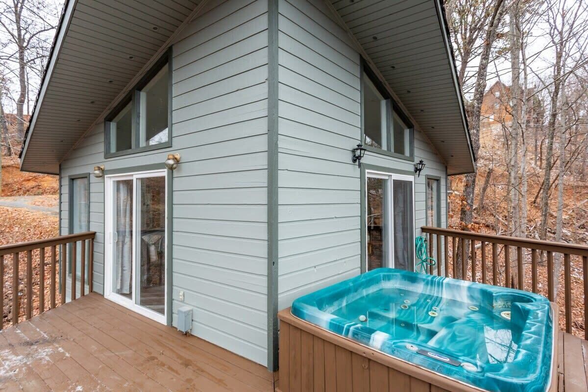Una casa con jacuzzi en el porche, terraza cubierta y vistas a árboles y un edificio al fondo.