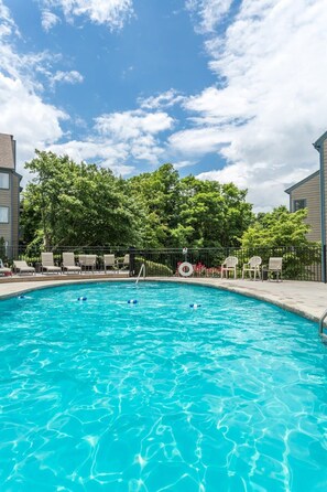 A swimming pool with clear blue water, surrounded by lounge chairs and a fence.