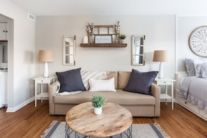 Un salon avec un canapé beige, deux tables d’appoint, une table basse ronde et une étagère décorative placée au-dessus.