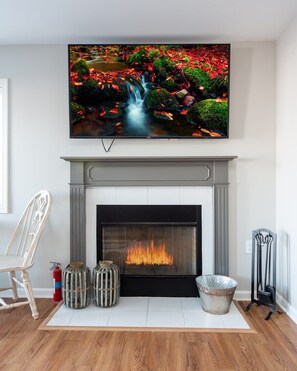 A living room with a fireplace, a television mounted above it, and a wooden floor.
