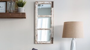 Sala de estar em tons neutros com sofá, abajur e um espelho decorativo.