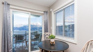 Een kamer met een ronde tafel, stoelen, een potplant en uitzicht op een besneeerd landschap door een glazen deur.
