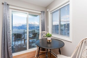 A room with a round table, chairs, a potted plant, and a view of mountains through a glass door.
