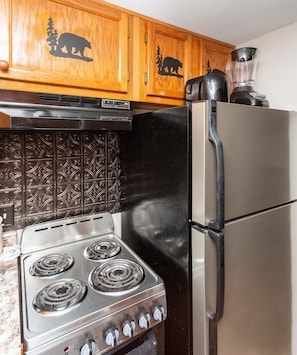 A kitchen with a stove, refrigerator, and wooden cabinets with bear designs. - Amazing Views Of Mt. LeConte/Indoor Pool & Hot Tub (Gatlinburg)