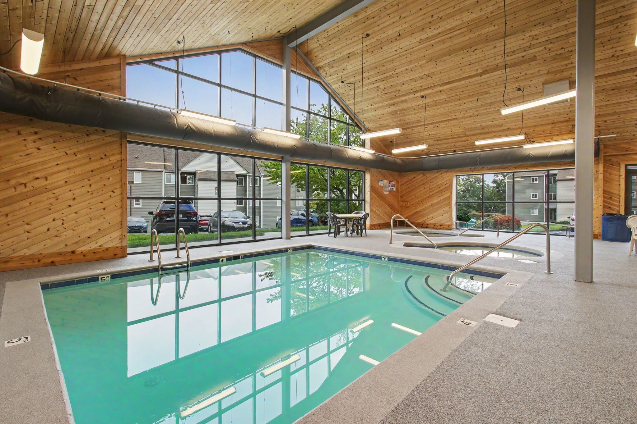 An indoor swimming pool with clear glass walls, wooden ceiling, and a view of the outside.
