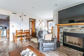 Un soggiorno con camino, televisore, zona pranzo con tavolo e sedie, e cucina visibile attraverso una porta aperta.