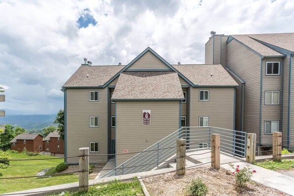 A multi-story residential building with a fire escape, a gated entrance, and a view of the surrounding landscape.