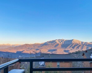 A mountain range with a clear sky, a wooden building with a sloped roof, and a metal railing in the foreground.