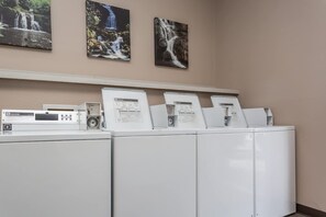 A laundry area with a washing machine, dryers, and informational posters on the wall.