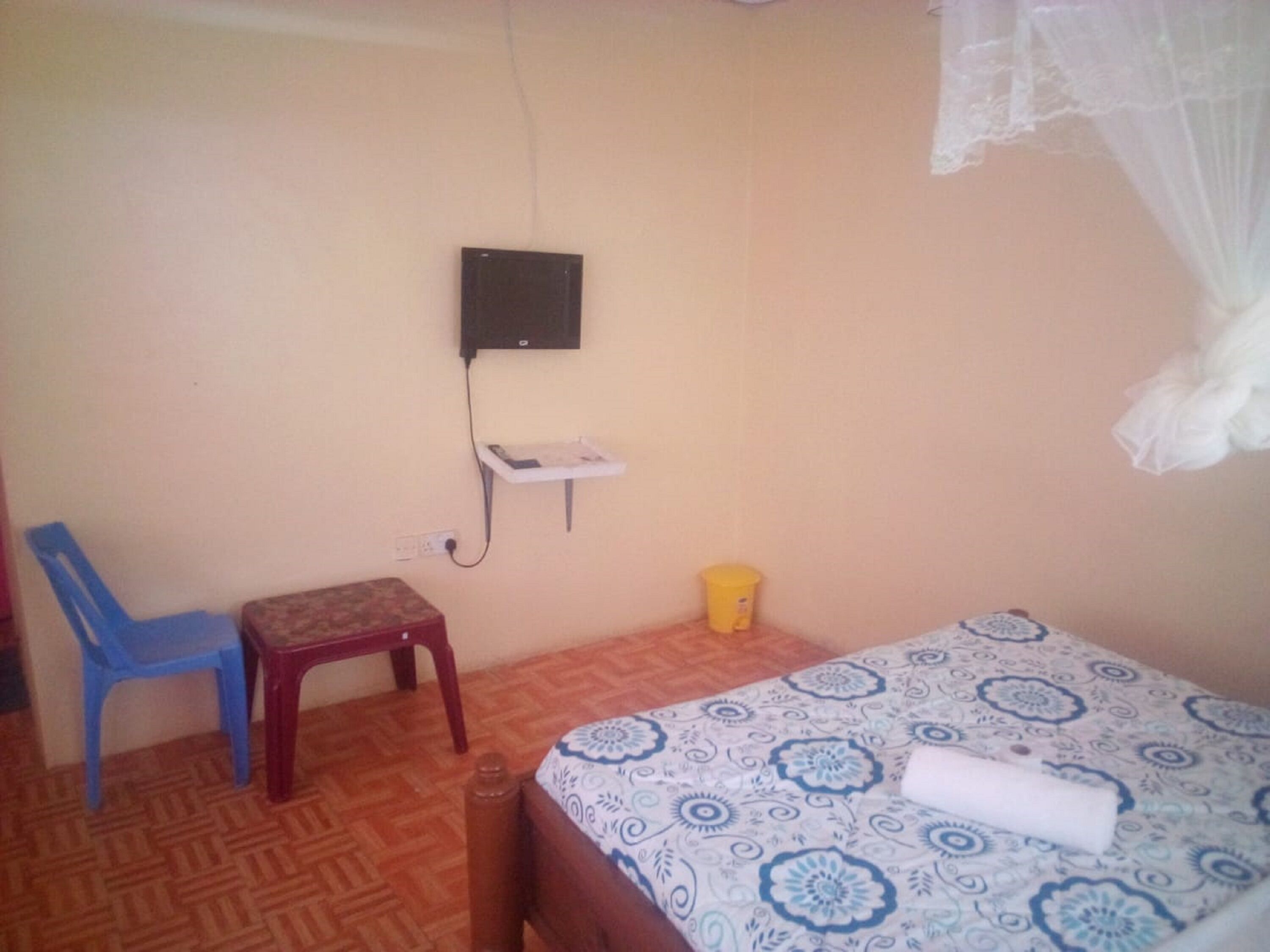 Un dormitorio con una cama, una silla, una mesita pequeña, una mesita de noche y un enchufe en la pared.