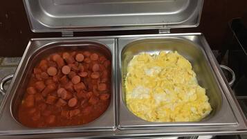 A buffet with two trays: one with sliced sausages and the other with scrambled eggs.