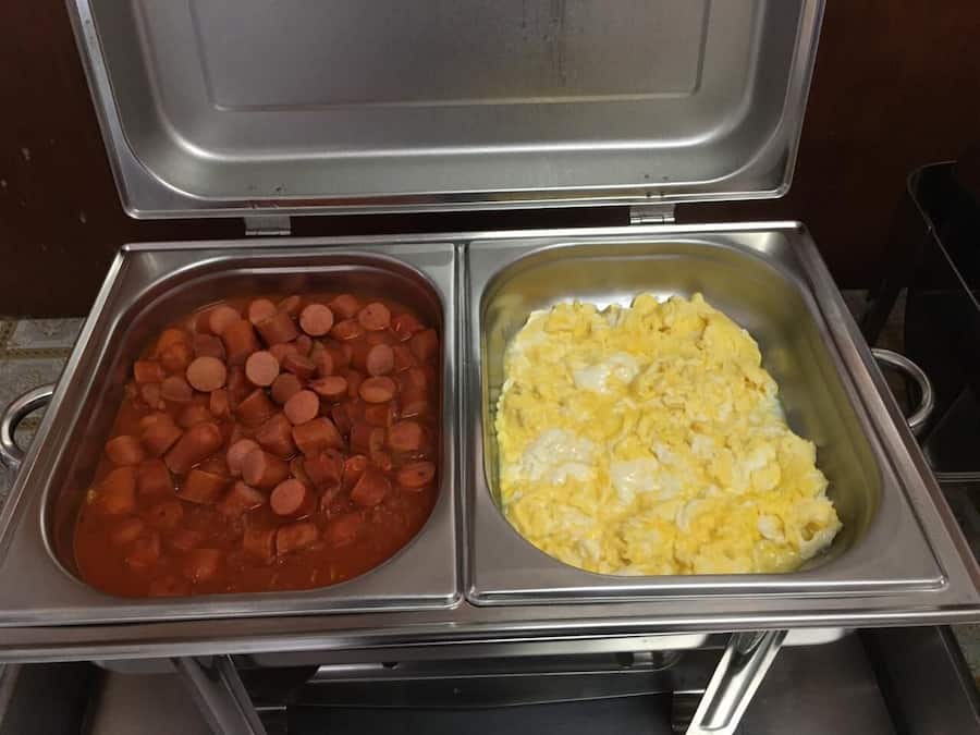A buffet with two trays: one with sliced sausages and the other with scrambled eggs.