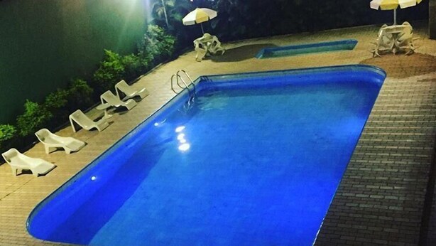Una piscina rectangular con un borde empedrado, rodeada de sillas reclinables blancas y sombrillas.